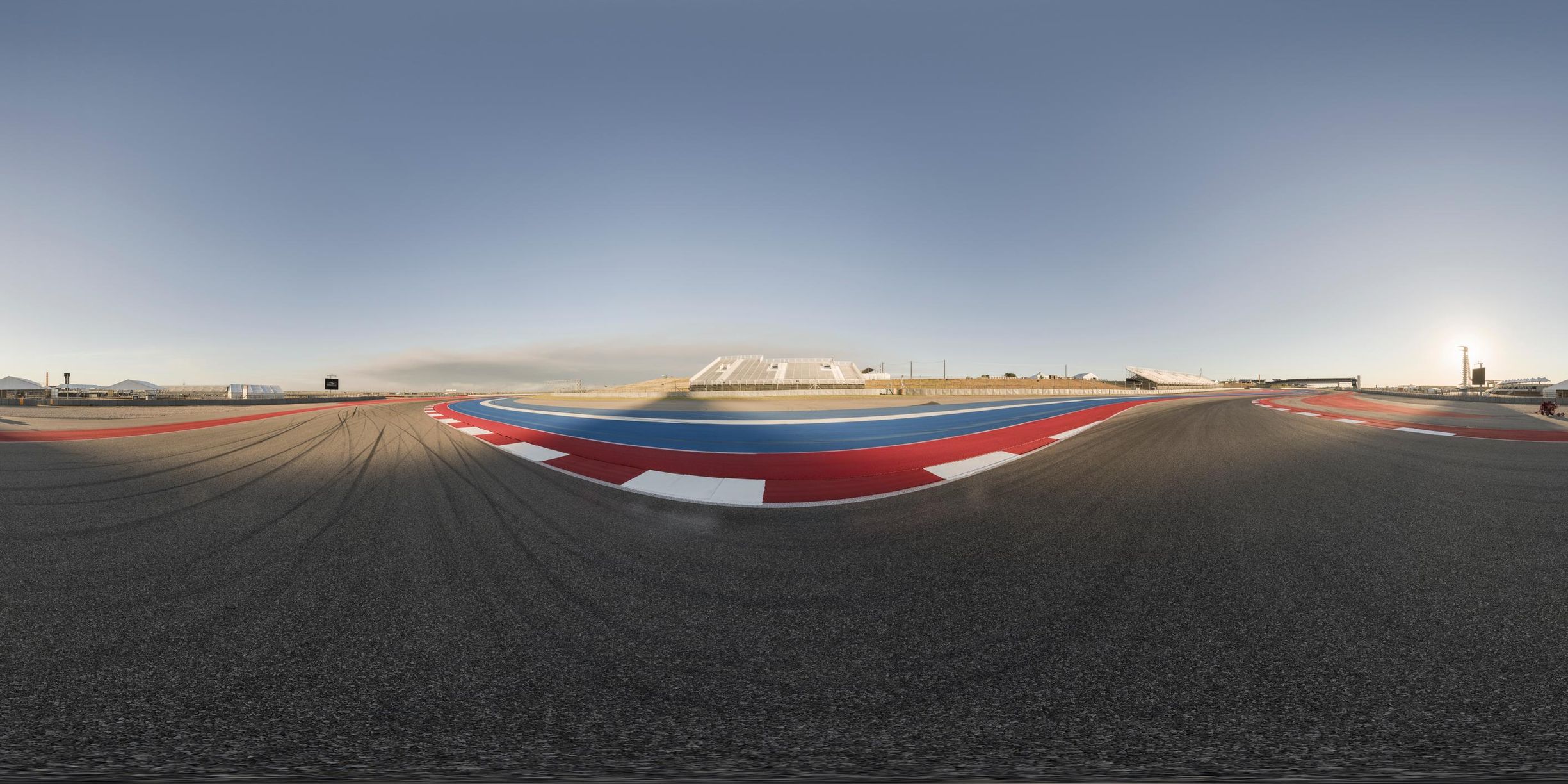 a view of an open race track from a fish eye lens in midair with a person riding a motorcycle