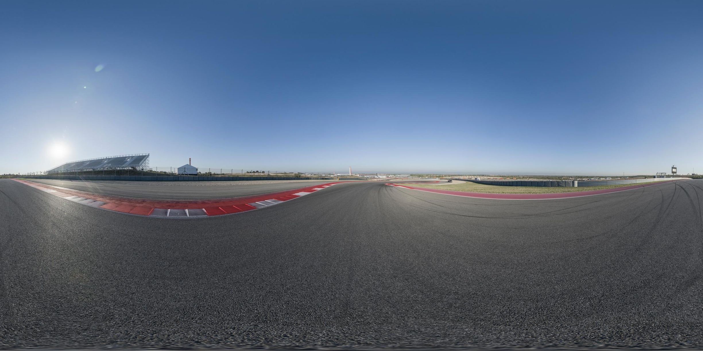 an empty race track is shown from the side on a sunny day with blue sky
