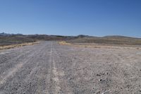 a long dirt road leading to the mountains with some rocks on both sides and gravel in the foreground