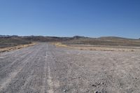 a long dirt road leading to the mountains with some rocks on both sides and gravel in the foreground