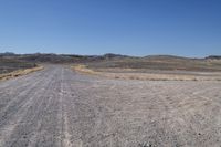 a long dirt road leading to the mountains with some rocks on both sides and gravel in the foreground