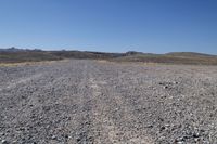 a long dirt road leading to the mountains with some rocks on both sides and gravel in the foreground