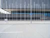 the glass facade is reflecting the sky and poles with traffic signs nearby it, and the parking lot has only one sign on the pole in front