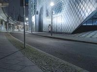 a city street with modern buildings on either side of it at night, and one person walking in front of the building at the end