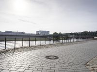 brick walkway between two bridges over river next to building complex with street lights on, city bridge in distance