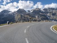 an open road on a windy day with mountains in the background and some snow on the top