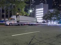 a white semi truck traveling down the street at night in a city setting that seems to be turning left