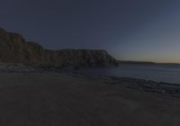 an ocean beach at sunset with rocks and a cliff face in the background on a clear day