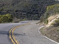 an empty road on a steep mountain side with two yellow stripes on the one side