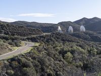 several telescopes on top of a mountain and in the air above them, near an open road