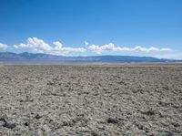 a barren, vast plain in the desert under a blue sky with mountains in the distance