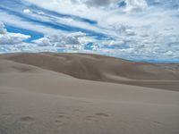 large dunes in an area that is vast and covered in sand under the blue sky with clouds