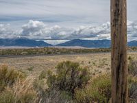 two wooden telephone poles on the side of road with mountains in the background and clouds in the sky