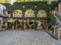 a brick walkway with stairs and ivy growing over the staircases and a building that has a courtyard below