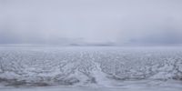 the surface of an icy ice covered field with a mountain in the background and fog