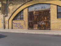 a closed down building is seen on a street side walk outside of some buildings, with graffiti all over it