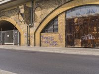 a closed down building is seen on a street side walk outside of some buildings, with graffiti all over it