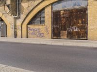 a closed down building is seen on a street side walk outside of some buildings, with graffiti all over it