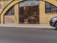 a closed down building is seen on a street side walk outside of some buildings, with graffiti all over it