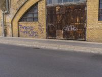 a closed down building is seen on a street side walk outside of some buildings, with graffiti all over it