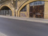 a closed down building is seen on a street side walk outside of some buildings, with graffiti all over it