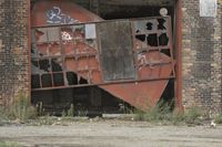 a fire hydrant is standing outside of a broken down warehouse door with graffiti on it