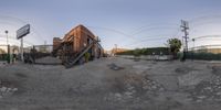 an abandoned building sitting in the dirt of an industrial setting with electric wires and barbed wire