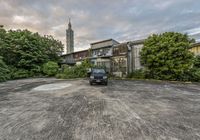 an abandoned building with a pickup truck in front of it and trees around the parking lot