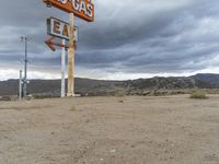 an abandoned sign for an old - fashioned gas station sits in the sand at dusk