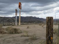 an abandoned intersection in the middle of a deserted desert area on a cloudy day with mountains in the distance