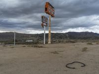 an abandoned intersection in the middle of a deserted desert area on a cloudy day with mountains in the distance