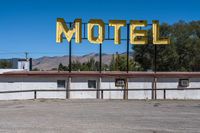 a motel sign is standing out in an abandoned place, with mountains in the background