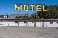 a motel sign is standing out in an abandoned place, with mountains in the background