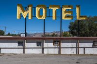 a motel sign is standing out in an abandoned place, with mountains in the background