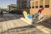 an abstract sculpture sitting on the side of a road next to buildings on a bridge