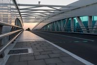 a pedestrian walkway crossing the side of a road next to a building at sunset, with lights from traffic lights