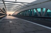 a pedestrian walkway crossing the side of a road next to a building at sunset, with lights from traffic lights