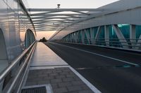 a pedestrian walkway crossing the side of a road next to a building at sunset, with lights from traffic lights