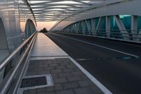 a pedestrian walkway crossing the side of a road next to a building at sunset, with lights from traffic lights