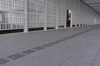 a long white wall covered with a latticed area of bricks and glass blocks on the ground