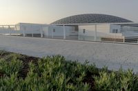 a white building next to green grass and plants in front of the building, which appears to have many different structures