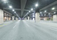 an empty street with lots of lights on the overhead ceiling in a building area at night