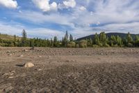 a dirt field and rocks sitting under clouds above the ground with trees on both sides