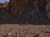 a red motorcycle riding on the rocky road near a hill of rocks and a person