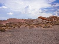 a dry desert landscape in the middle of a valley with rocks and brush, clouds in the background