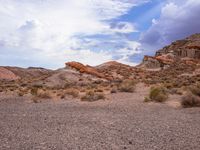 a dry desert landscape in the middle of a valley with rocks and brush, clouds in the background