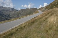 a motorcycle is driving down a winding road in the middle of mountains on an extremely sunny day