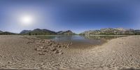 a panorama view of the beach from the water, with mountains in the distance, and blue skies and sun