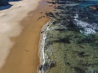 an aerial view of a beach and some rocks in the water and a person on the sand with a surfboard