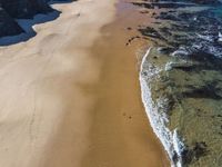 an aerial view of a beach and some rocks in the water and a person on the sand with a surfboard